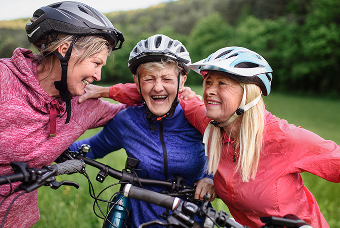 Three women wearing bike helmets and active clothing, laugh together